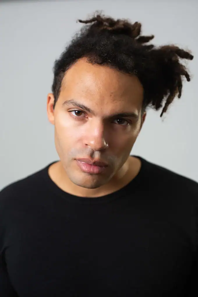 Headshot example featuring a minimalist close-crop portrait of a man with an intense, direct gaze and natural hair texture, set against a neutral gray background to emphasize personal brand identity.