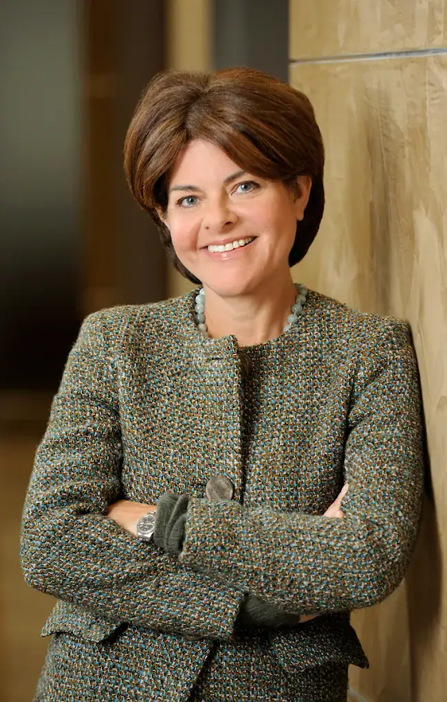 Headshot example featuring a woman in a high-quality tweed jacket leaning against a warm, rich-toned textured wall, conveying longevity and gravitas.