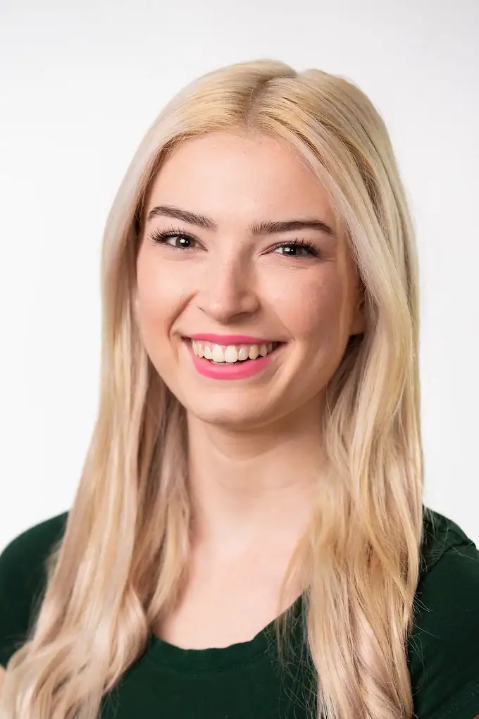 Headshot example featuring a blonde woman with a warm, enthusiastic open-mouthed smile, wearing a dark green top with bright pink lipstick against a pure white high-key background for maximum clarity.