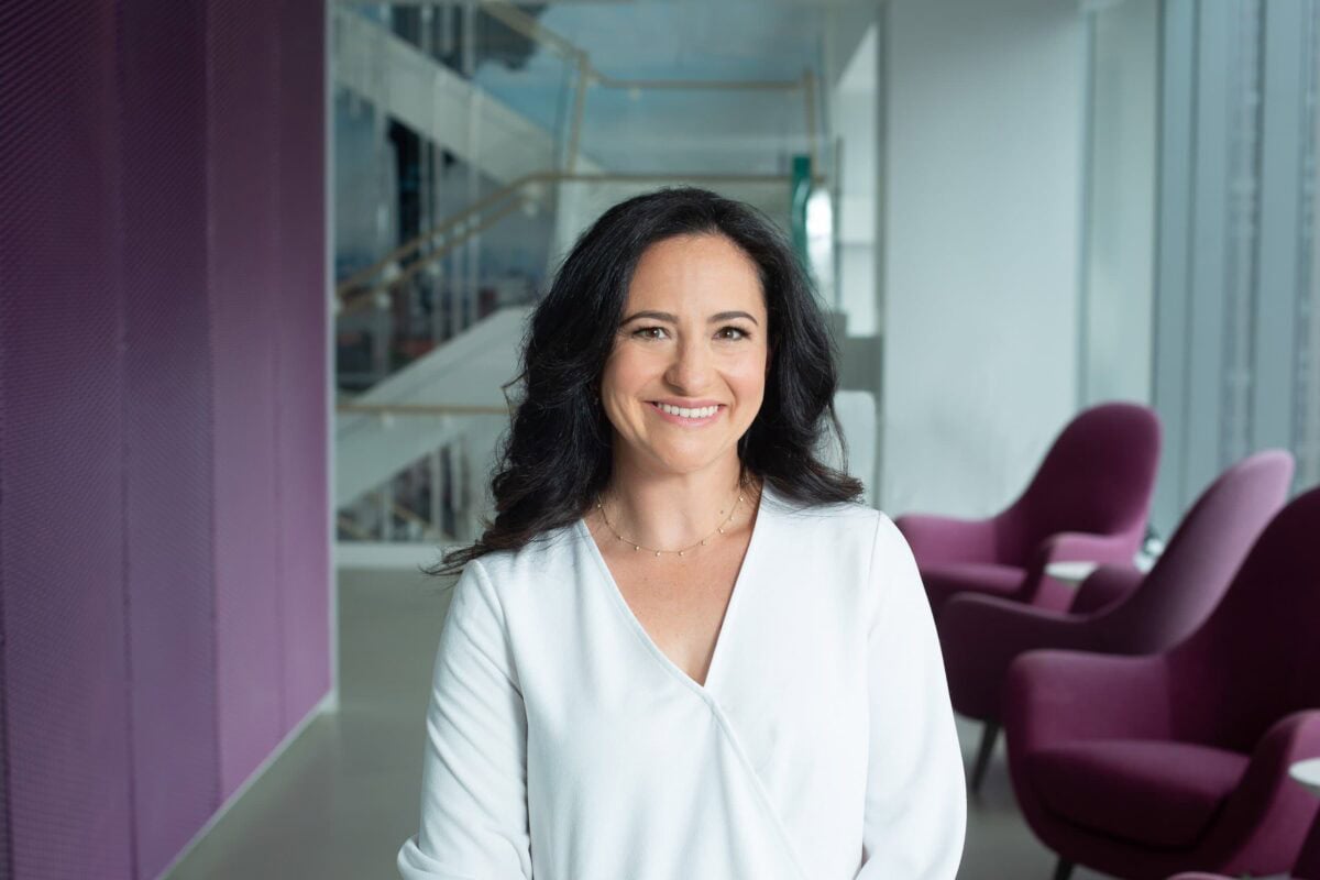 Headshot example featuring a woman in a white top standing in a modern office, contrasted against bold purple seating and architectural office elements.