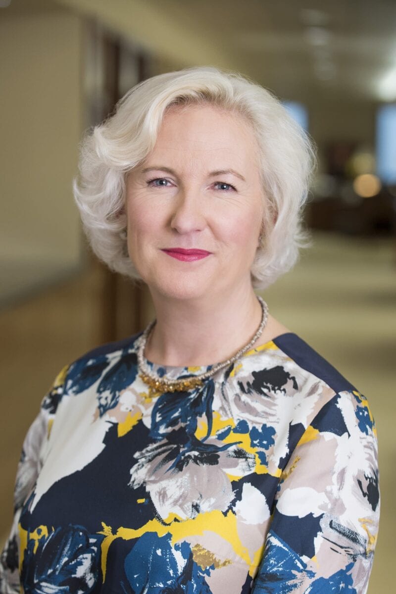 Headshot example featuring a woman in a colorful, patterned top with a warm expression, using a shallow depth of field to create soft focus background isolation.