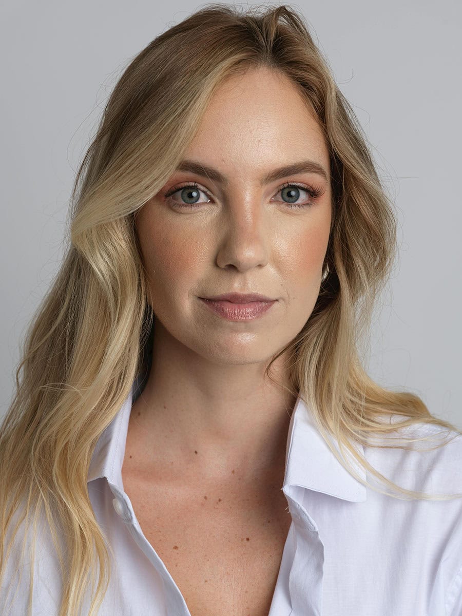Headshot example featuring a woman with blonde hair in a crisp white open-collared shirt, utilizing soft directional lighting and a neutral gray backdrop for a clean, minimalist aesthetic.