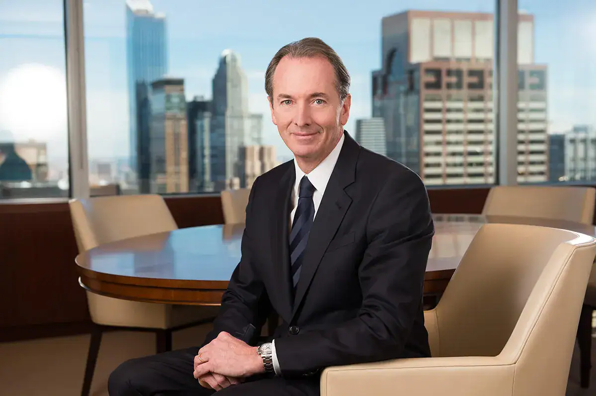 A professional individual sits comfortably in a high-rise office chair next to a large window showcasing a panoramic view of the New York City skyline.